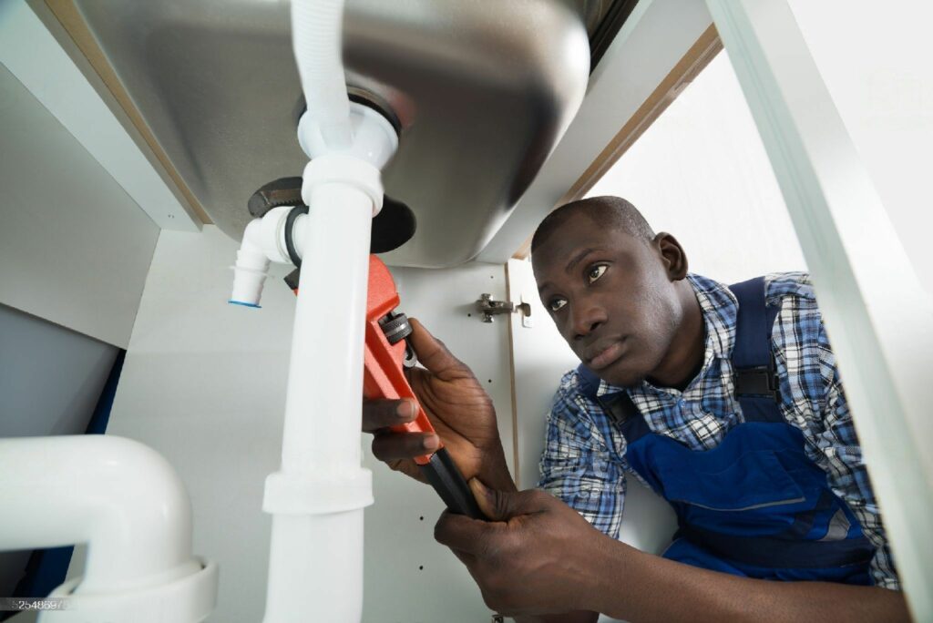 Young African Handyman Repairing Sink Pipe With Worktool